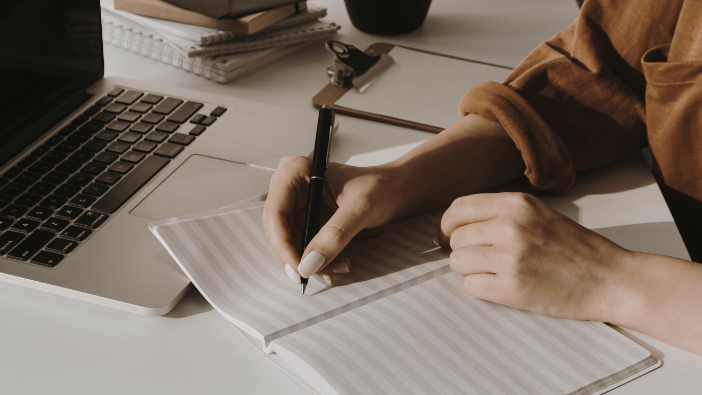 Close-up of a person writing notes next to a laptop, symbolizing planning and storytelling strategies and branding for startups.