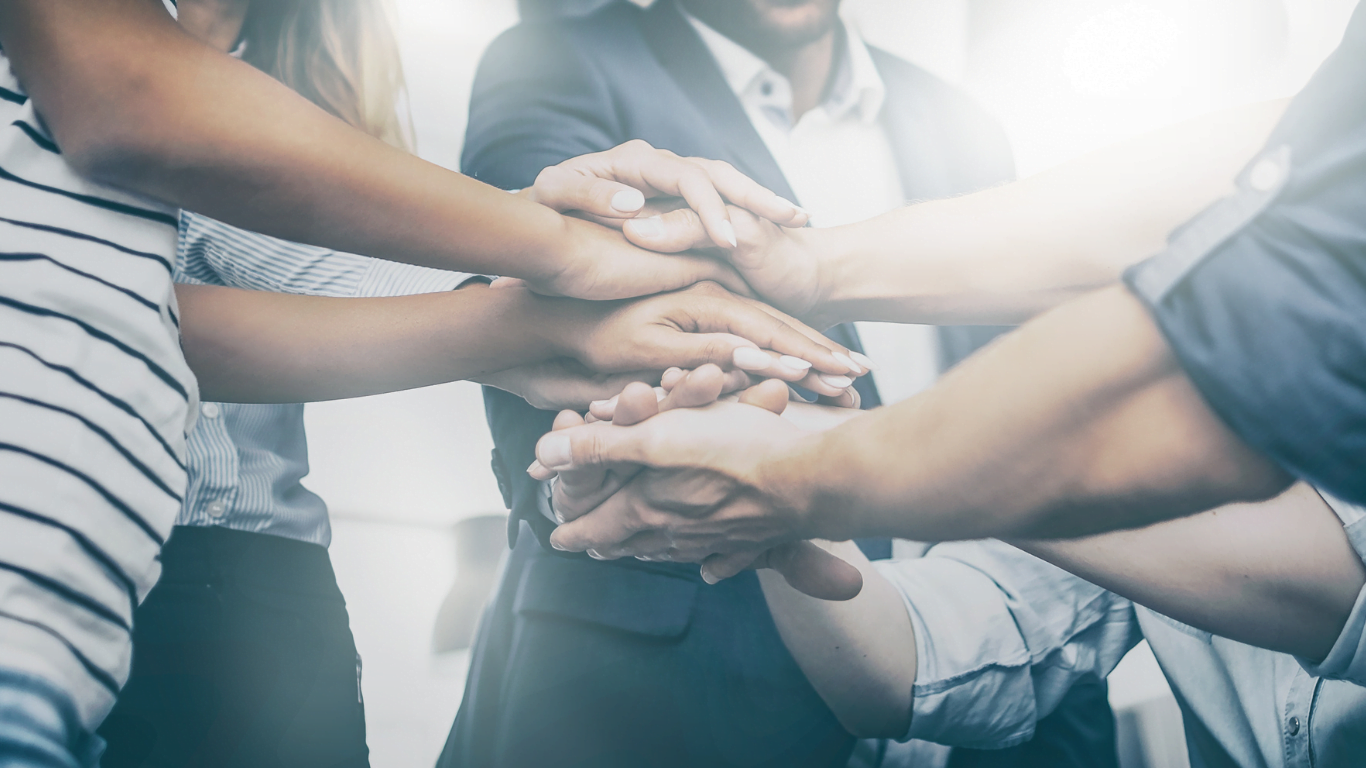 Close-up of a group of people stacking hands in a symbol of unity and teamwork, illustrating the strength of community in purpose-driven branding.